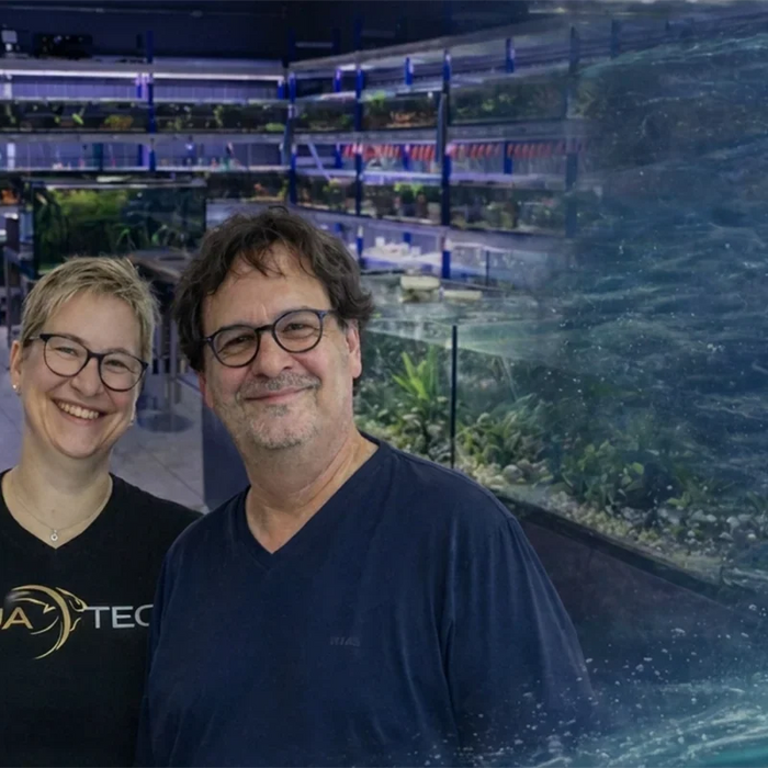 Zwei lächelnde AQUA TECK-Teammitglieder stehen im Verkaufsraum mit beleuchteten Aquarien im Hintergrund, Titel „Ein Blick hinter die Kulissen von AQUA TECK