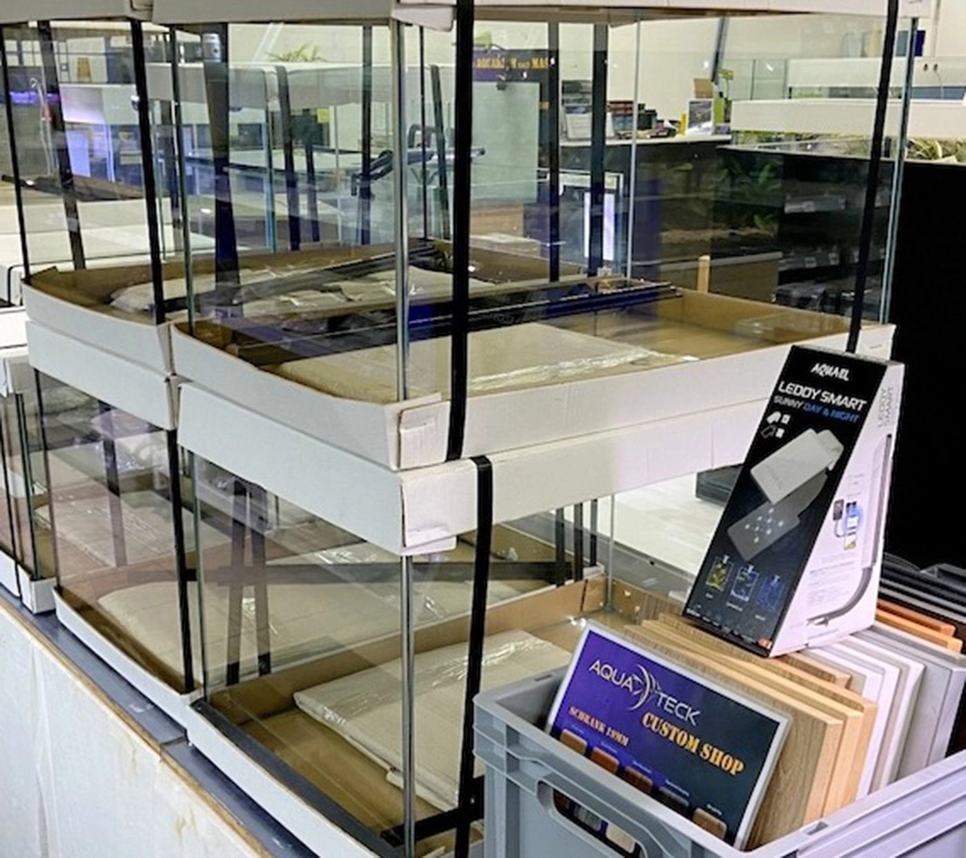 Gestapelte leere Aquarien im Verkaufsraum, davor eine LED-Beleuchtung und ein Aufsteller für den AQUA TECK Custom Shop.